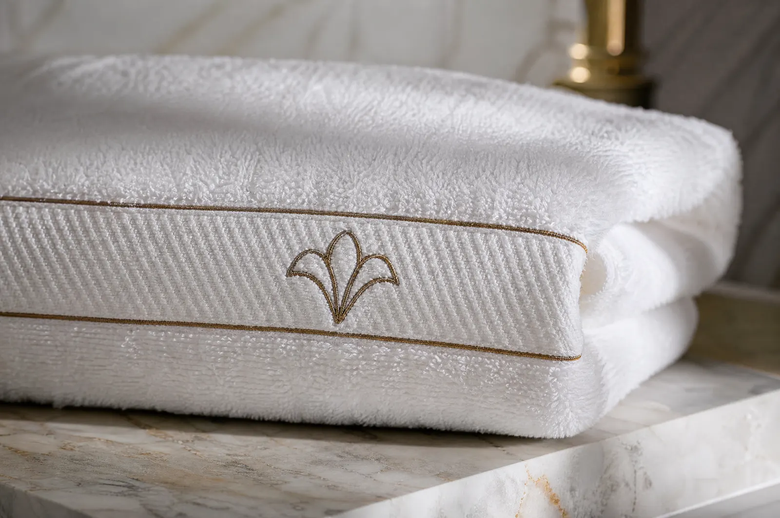 A plush white towel with a gold embroidered band and emblem